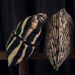 Twee Elitis-sierkussens met zebra- en tijgerprint leunen tegen elkaar op een houten bank voor een donkere achtergrond.
