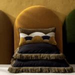 Sierkussens uit de Elitis najaarscollectie 2024, model Honore en Jane, gestyled tegen een okergele stoffen achterwand.