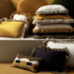 Stapel Elitis-sierkussens in warme herfsttinten met franjes in een sfeervolle interieursetting voor najaar 2024.