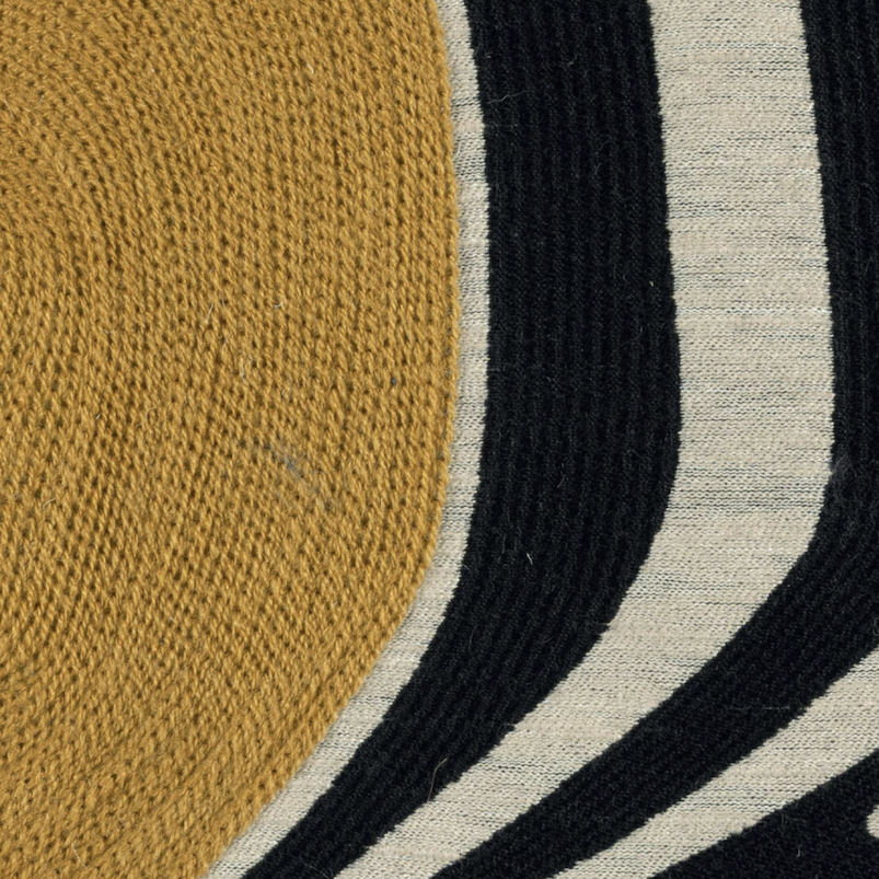 Detailopname van de Elitis-stof Onde LZ 865 22 met een geweven patroon in okergeel, zwart en beige.