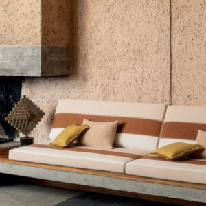 Bank bekleed met Elitis-stof Rosarito LR 356 35 in een warme, moderne interieursetting met betonnen haard.