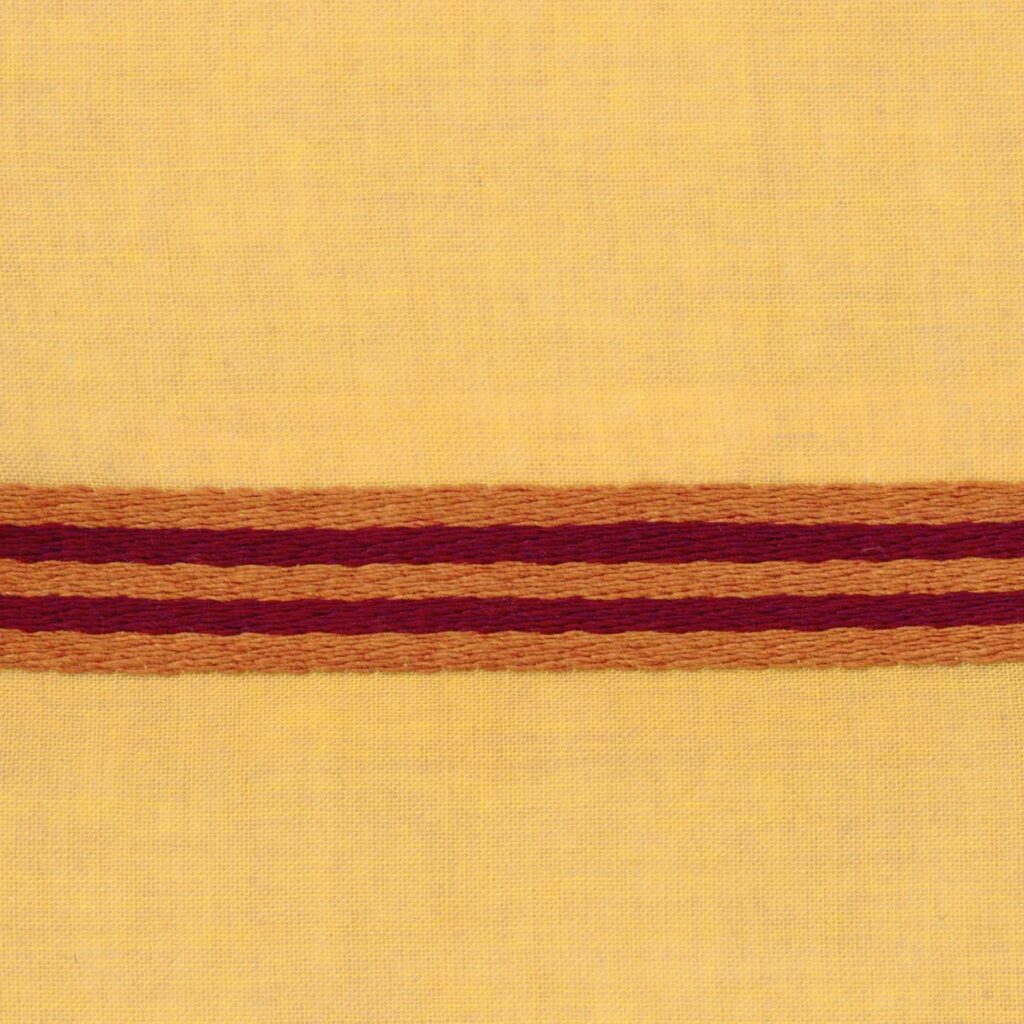 Geel Elitis-stof Acosta Casilda met horizontale borduursels in rood- en oranjetinten.
