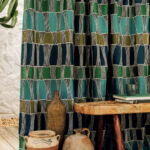 Gordijn van Elitis-stof Acosta Santa Cruz in blauwtinten met geometrisch patroon, naast een houten tafel met aardewerken potten en boeken.