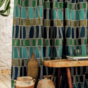 Gordijn van Elitis-stof Acosta Santa Cruz in blauwtinten met geometrisch patroon, naast een houten tafel met aardewerken potten en boeken.