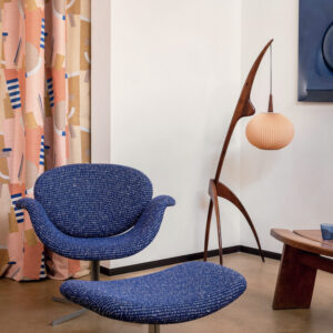 Moderne interieurhoek met een blauw gestoffeerde Elitis-stoel en bijpassende hocker, voor kleurrijke Alchimia Intreccio gordijnen.