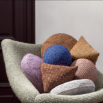 Stijlvolle Elitis Alchimia Intreccio-kussens in diverse kleuren en vormen liggen in een moderne stoffen fauteuil.
