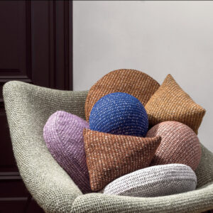 Stijlvolle Elitis Alchimia Intreccio-kussens in diverse kleuren en vormen liggen in een moderne stoffen fauteuil.
