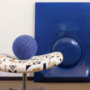 Moderne interieursetting met een Elitis-stof beklede stoel, een blauwe bol en een groot blauw kunstobject op de achtergrond.