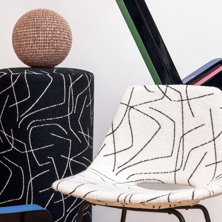 Designstoel en poef bekleed met Elitis Alchimia Scala-stof met abstracte zwarte lijnen op een witte en zwarte achtergrond.