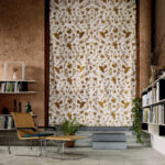 Interieur met een Elitis Comala LZ 891 31 stofgordijn met goudbruine botanische print, omgeven door boekenkasten en een rotan loungestoel.