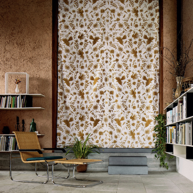 Interieur met een Elitis Comala LZ 891 31 stofgordijn met goudbruine botanische print, omgeven door boekenkasten en een rotan loungestoel.