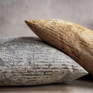 Twee decoratieve Elitis-kussens van de stof 'Craft Chic Antico' met een gemêleerd patroon in aardetinten en grijs.