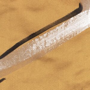 Detail van Elitis-stof Craft Chic Istinto LF 344 21 met een okergele textielbasis en abstracte penseelstreken in wit en zwart.