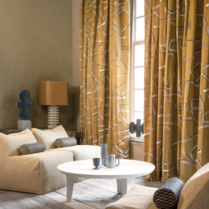 Gezellige zithoek met Elitis gordijnen in het patroon Craft Chic Istinto LF 344 21 in okergeel, gecombineerd met neutrale meubels en moderne accenten.
