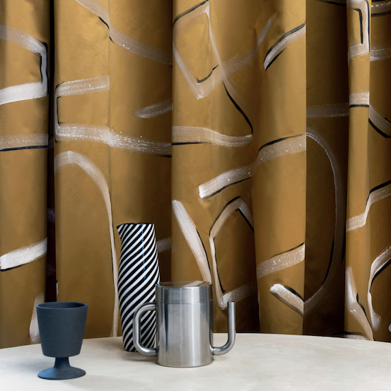 Gouden Elitis-stof Craft Chic Istinto LF 344 21 met abstract patroon, gecombineerd met moderne accessoires op een tafel.