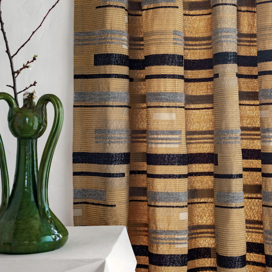 Goudbruine Elitis Craft Chic Regina LR 335 05 stof met horizontaal gestreept patroon als gordijn, naast een groene decoratieve vaas.