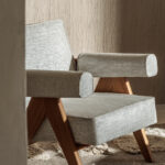 Moderne fauteuil bekleed met Elitis-stof Ephemere Aube LI 897 05 en houten poten, in een warme interieurruimte.