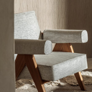 Moderne fauteuil bekleed met Elitis-stof Ephemere Aube LI 897 05 en houten poten, in een warme interieurruimte.