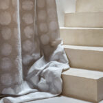 Lichtgrijze Elitis-stof Ephemere Full Moon LI 894 05 met cirkelpatroon hangt langs een beige trap.
