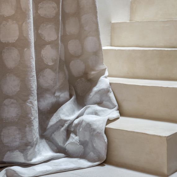 Lichtgrijze Elitis-stof Ephemere Full Moon LI 894 05 met cirkelpatroon hangt langs een beige trap.