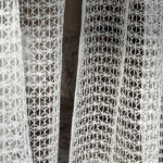 Wit doorschijnend Elitis Ephemere Minato LW 905 01 gordijn met een fijn geometrisch borduurpatroon.