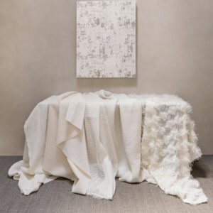 Een elegante sfeeropstelling met diverse Elitis Ephemere Patchi Li 901-01 stoffen in crèmekleurige texturen gedrapeerd over een tafel tegen een neutrale achtergrond.