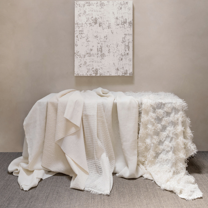 Een elegante sfeeropstelling met diverse Elitis Ephemere Patchi Li 901-01 stoffen in crèmekleurige texturen gedrapeerd over een tafel tegen een neutrale achtergrond.