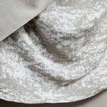 Detail van de Elitis-stof Ephemere Yeso LI 898 03 met een lichtgrijze en witte textuur in een gevouwen patroon.