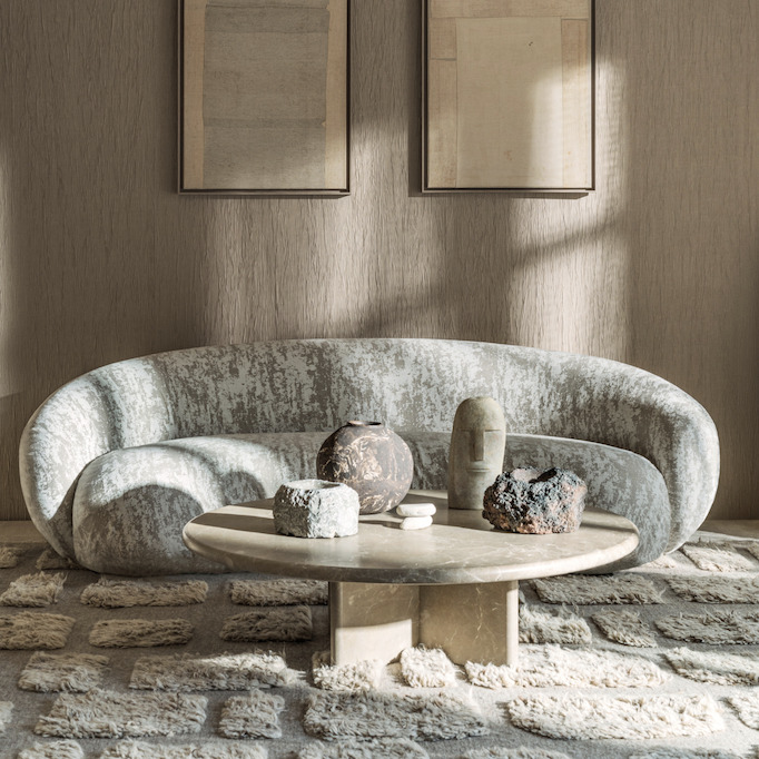 Moderne zithoek met een Elitis Ephemere Yeso LI 898 03 beklede bank, een ronde stenen salontafel en decoratieve objecten in aardetinten.