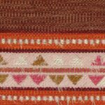 Detailopname van de kleurrijke Elitis-stof Escondido Alma WO 114 35 met geweven patronen in rood, roze, wit en bruin.