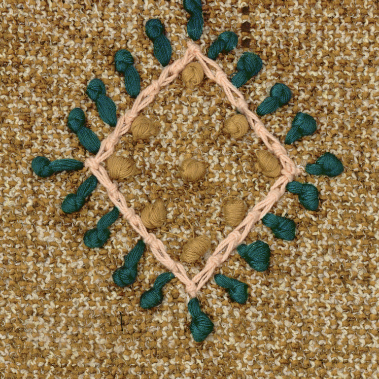 Detail van Elitis-stof Loreto LZ 890 79 met geborduurd ruitpatroon in beige, groen en okergeel garen op een grofgeweven bruine achtergrond.
