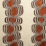 Decoratieve Elitis-stof Escale LI 865 35 met symmetrisch patroon van organische vormen in bruin- en roesttinten op een beige achtergrond.