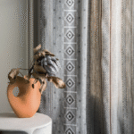 Een terracotta vaas met een gedroogde bloem staat voor een gordijn van Elitis-stoffen met geometrisch patroon in neutrale tinten.