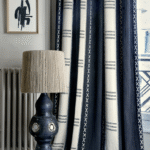 Donkerblauwe en crèmekleurige Elitis Escale-gordijnen met etnisch patroon naast een decoratieve lamp en abstracte wandkunst in een stijlvolle interieurhoek.
