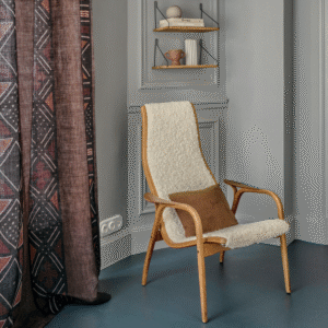 Stijlvol interieur met Elitis Escale gordijn, een houten loungestoel met zachte bekleding en wandplank met decoratieve objecten.