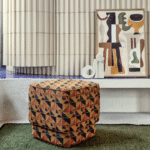 Gestoffeerde poef met Elitis Horizon-stof in geometrisch patroon, voor een modern interieur met kunst en sculpturen.