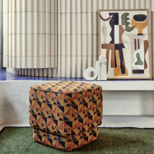 Gestoffeerde poef met Elitis Horizon-stof in geometrisch patroon, voor een modern interieur met kunst en sculpturen.