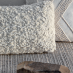 Twee decoratieve Elitis Horizon-kussens in neutrale tinten op een geweven vloerkleed.