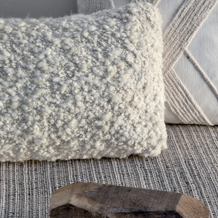 Twee decoratieve Elitis Horizon-kussens in neutrale tinten op een geweven vloerkleed.