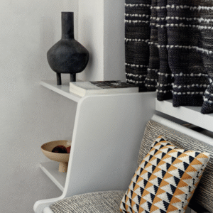 Moderne zithoek met Elitis Horizon-stoffen, een grafisch sierkussen en stijlvolle accessoires op witte wandplankjes.