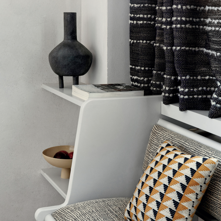 Moderne zithoek met Elitis Horizon-stoffen, een grafisch sierkussen en stijlvolle accessoires op witte wandplankjes.