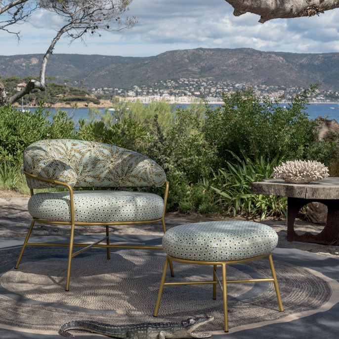 Luxe Elitis outdoor-stoel met bijpassende hocker in een mediterrane tuinsetting met uitzicht op de kust.