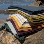 Stapels Elitis City linnenstoffen in diverse kleuren liggen op een rots aan het water.