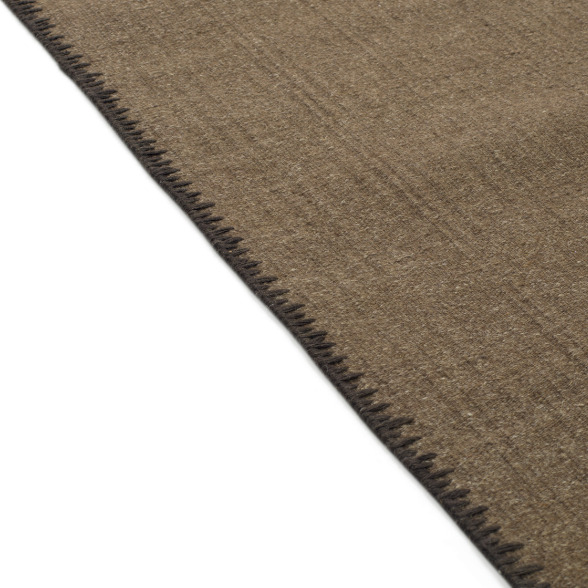 Detailopname van de rand van het Elitis Tenere vloerkleed TA 126 18 met zichtbare stiksels.