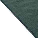 Detailopname van de rand van het donkergroene Elitis Tenere vloerkleed TA 126 64 met fijne weefstructuur.