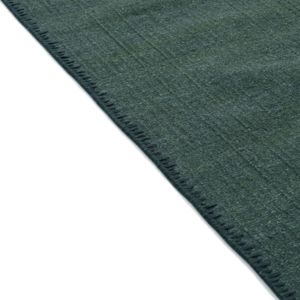 Detailopname van de rand van het donkergroene Elitis Tenere vloerkleed TA 126 64 met fijne weefstructuur.