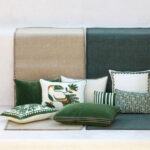 Decoratieve kussens in groentinten liggen op een Elitis Tenere vloerkleed in beige en groen, tegen een lichte achtergrond.