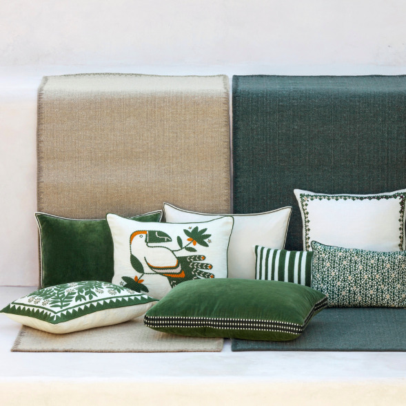 Decoratieve kussens in groentinten liggen op een Elitis Tenere vloerkleed in beige en groen, tegen een lichte achtergrond.
