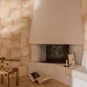 Moderne zithoek met een abstracte open haard, houten meubelen en Elitis Tribus Comporta RM 1079 01 behang.