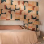 Sfeervolle slaapkamer met Elitis Tribus Comporta RM 1079 60 behang in warme aardetinten achter een bed met beige beddengoed.